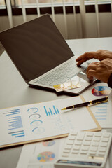 Young businessman analyzing business graph documents on desk with laptop computer and calculator Business and economic concepts with vertical images.