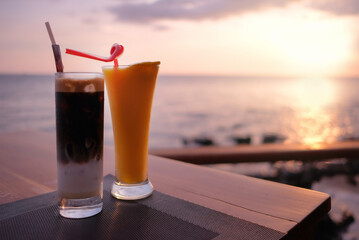 Iced Vietnamese coffee and orange juice on table, at bar restaurant balcony, sea facing, sunset in background. Beautiful relaxing mood in evening, at tropical resort in Asia