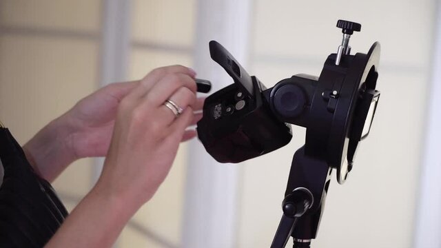 Girl photographer changes batteries in flash for camera. External studio light.