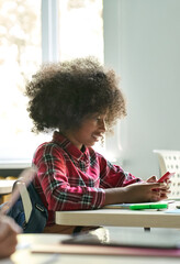 Fototapeta na wymiar Happy smiling African American teen elementary schoolgirl holding cell phone smartphone sitting in classroom using mobile apps for learning. Modern technologies for education concept. Vertical.