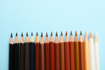 Colorful pencils on light blue background, flat lay with space for text. Stop racism