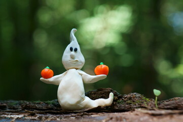 A toy ghost made of plasticine close-up. In the hands of the ghost holds a pumpkin.