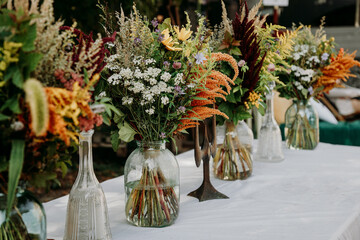 Rustic style. Boho style bouquets on the table in glass vases and jars. Wooden table and white...