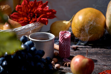 Rustic natural cozy still life of mug of tea, fruits, hazelnuts and cinnamon sticks. Autumn aesthetic concept, red georgine. Cozy home with warm tea and aromatic candle. Thanksgiving Day concept.