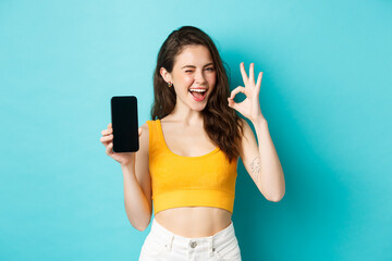 Attractive modern woman in summer clothes, winking assuringly, showing okay sign with blank...