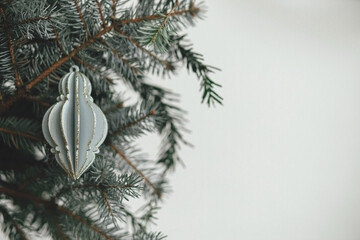 Merry Christmas! Stylish christmas ornament on fir branch close up. Space for text. Modern wooden...