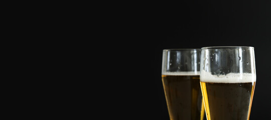 Two frosty glasses of cold golden beer with bubbles on the black background. Free space for text,...