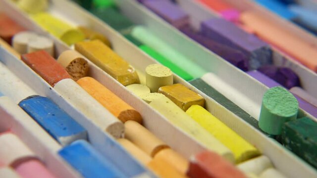 Multi-colored crayons of the various types, shapes and sizes lay out in separate cells in a box for storing crayons. Turntable, slow motion