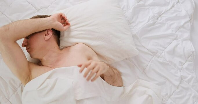 Young man tosses and turnes during sleep. Guy rolls over in bed. Restless sleep. Top view.