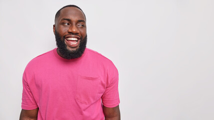 Handsome bearded man with dark skin dressed in casual pink t shirt laughs carefree shows optimism...