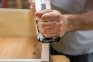 Closeup of man's hands using hand plane while woodworking.