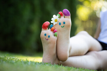 Children's feet with a pattern of paints smile on the green grass.