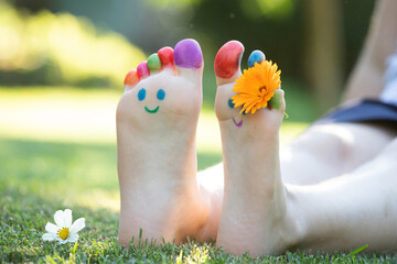 Fototapeta premium Children's feet with a pattern of paints smile on the green grass.