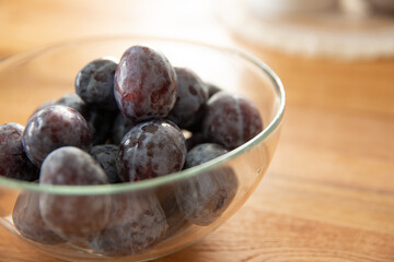 plums in a glass bowl on a wooden background. 