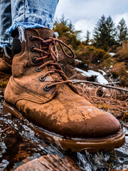 One wet cowboy boot stepping on the water in the mountains at winter season.