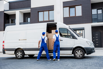 Two removal company workers unloading boxes from minibus into new home