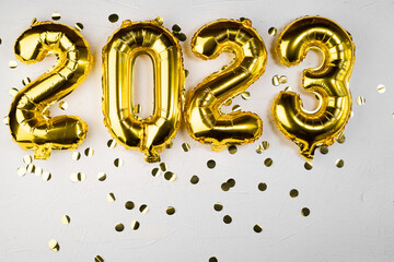 golden foil balloon 2023 New Year. Numbers two thousand twenty three from a foil figure on a gray cement background. Golden confetti and celebration. - obrazy, fototapety, plakaty