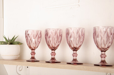 Wooden shelf table above a blurry kitchen window sill to display the product. On the shelf are crystal pink glasses with space for text