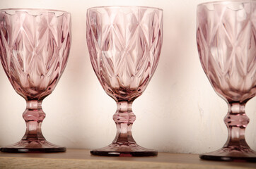 Wooden shelf table above a blurry kitchen window sill to display the product. On the shelf are crystal pink glasses with space for text