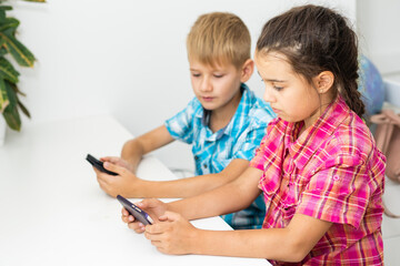 boy playing with smartphone next to his sister in the room at home.