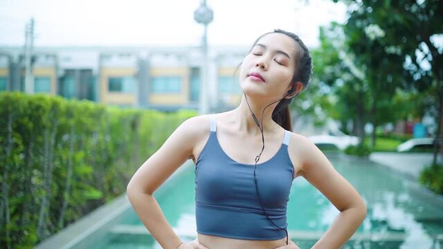 thai woman asian standing exercise neck rotation by the pool wearing headphones listening to music on smartphone concept health care fitness fitness person