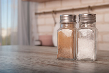 salt and pepper in a glass jar on a wooden table on a blurry background with space for text