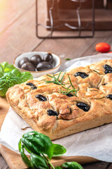 Traditional Italian Focaccia with black olives, herbs and oil on wooden table