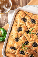 Traditional Italian Focaccia with black olives, herbs and oil on wooden table