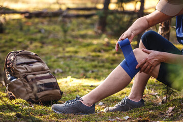 Injured hiker putting elastic bandage to her knee. Accident during hiking. Trekking first aid. Knee...