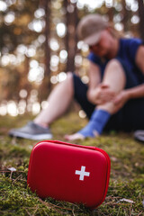 First aid kit and defocused injured tourist woman with sprain ankle in forest. Accident and injury...