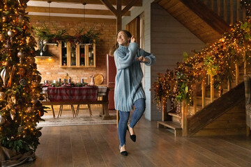 Happy millennial woman in comfort warm winter clothes having fun alone near Christmas tree, dancing...