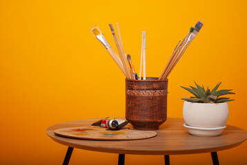 artistic brushes on a yellow background on a wooden table with paints and a palette with space for text isolated