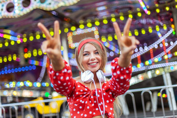 Happy cheerful blonde woman with headphones having fun in the amusement park