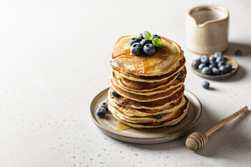 Stack of pancakes with syrup and blueberry on white textured background with copy space