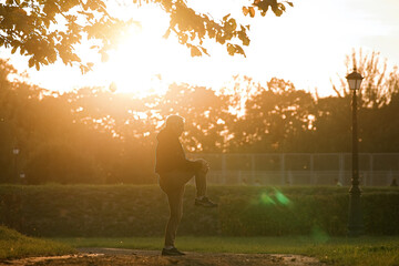 Mature sport man doing stretching warming up before running in autumn park during sunset     
