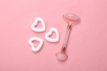 Jade face roller with hearts on pink background. Minimal beauty layout