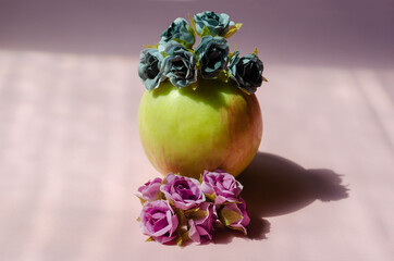 Green apple and artificial flowers on a pink background. Ripe fr
