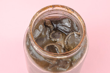 Botulism, food poisoning from canned foods concept. Glass jar with homemade pickled mushrooms in front of a pink. Spoiled black mushrooms at the top of an open jar