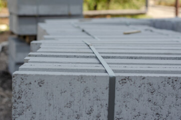 Obraz premium A stack of new gray boarders stacked on pallets. Concrete road barriers strapped together. Repair and construction work.
