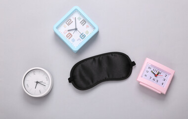 Sleep mask and many alarm clocks on gray background. Insomnia concept. Top view