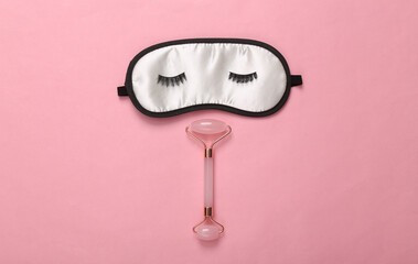 Beauty concept. Sleeping mask with eyelashes and massage roller for face on pink background. Top view