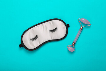 Beauty concept. Sleeping mask with eyelashes and massage roller for face on blue background. Top view