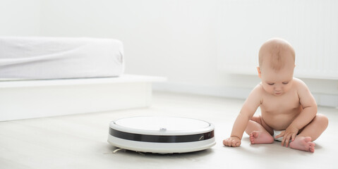 Little baby boy looks at the robotic vacuum cleaner at home.