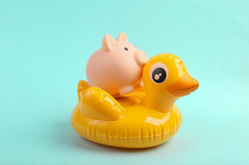 Inflatable yellow duck with piggy bank on blue background. Summer concept
