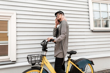 Fototapeta na wymiar Young beautiful woman with pink hairstyle and glasses in fashionable casual clothes with a bicycle standing near a wooden wall at home