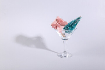 Christmas tree and gift box in cocktail glass on gray background. Creative idea. Minimal Christmas party concept.