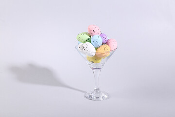 Cocktail glass with colored eggs on gray background. Creative idea. Minimal Easter concept. Concept art, layout