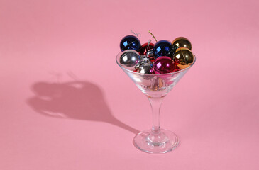 Cocktail glass with Christmas balls toys on pink background. Minimal Christmas party concept