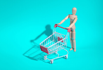 Wooden puppet with mini shopping cart on turquoise background