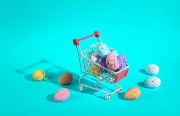 Mini shopping cart with colored easter eggs on turquoise background